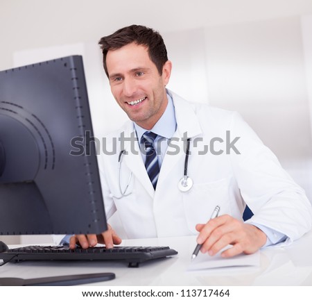 Smiling Medical Doctor With Stethoscope Sitting At A Desk