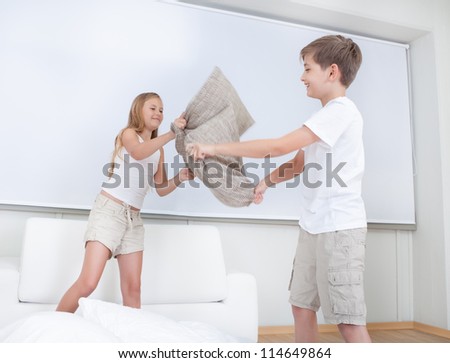 Siblings Having A Pillow Fight Together On Bed In Bedroom