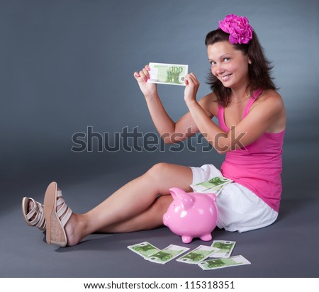 Beautiful happy woman with a cute expression saving for her retirement placing 100 euro bills in her large pink piggybank