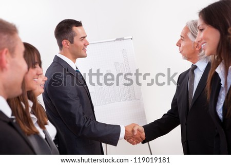 Two businessmen shaking hands in greeting and congratulations during an introductory line up of young staff in an office