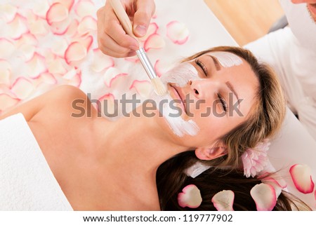 Beautician applying a face mask to a beautiful blonde woman lying relaxing in the salon with her eyes closed