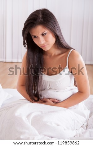 Woman with stomach pains from diarrhea or menstruation sitting up in bed clutching her abdomen and grimacing in pain