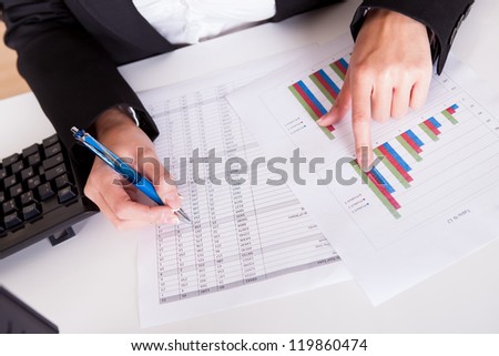 Overhead cropped image of female hands working with bar graphs and a spread sheet as she analyses data