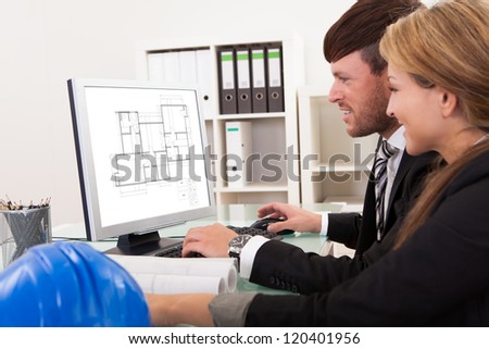 Two professional architects or structural engineers sitting at a desk looking at a computer discussing a building plan