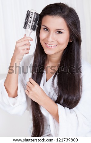 Beautiful woman sitting in a fresh white robe brushing her long straight brunette hair