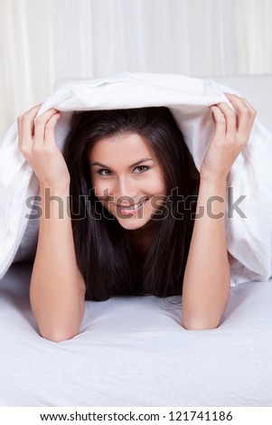 Smiling woman lying on her stomach on her bed under the bedclothes ...