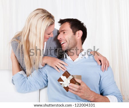 Smiling beautiful woman leaning over her husband\'s shoulder giving him a surprise gift