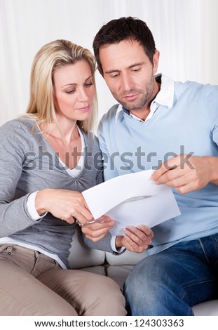 Woman about to cut up a document poised with the scissors at the ready while being watched by her husband