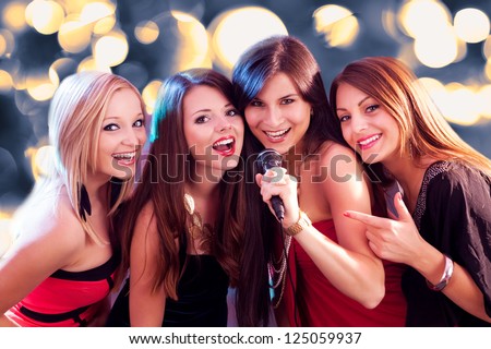 Four beautiful stylish girls singing karaoke at the club