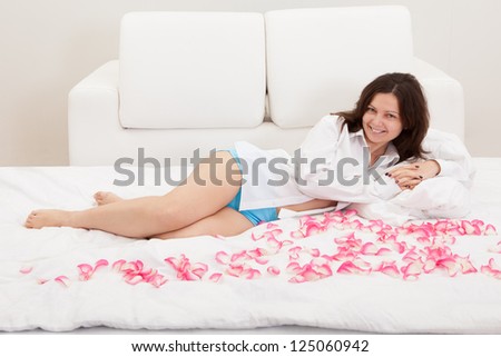 Smiling natural woman lying on a bed with her feet in the air surrounded by rose petals
