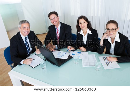 Overhead view of a group of diverse business executives holding a meeting around a table discussing graphs showing statistical analysis