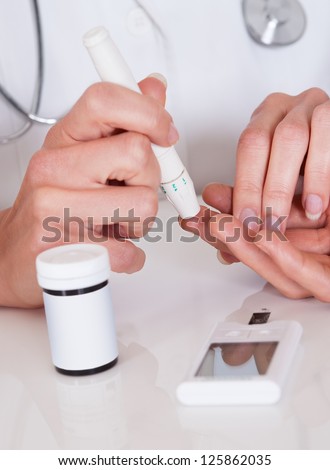 Doctor testing a patients glucose level after pricking his finger to draw a drop of blood and then using a digital glucometer