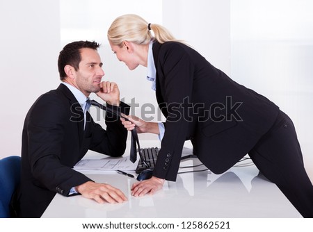 Flirting in the office as a beautiful blonde businesswoman pulls a colleague towards her by his tie