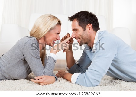 Young couple watching each other gazing into each others eyes with love while lying on their stomachs on a white carpet