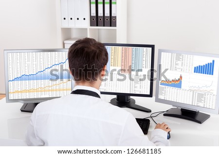 Over the shoulder view of the computer screens of a stock broker trading in a bull market showing ascending graphs