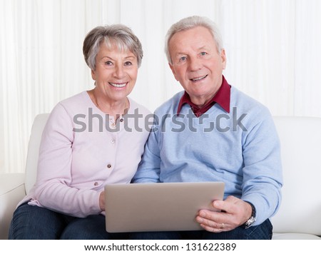 Senior Couple Sitting On Couch And Looking At Laptop Computer