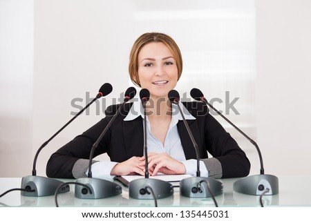 Young Cheerful Businesswoman Giving Speech In Conference