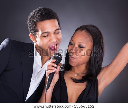 Portrait Of African Couple Singing With Microphone Over Grey Background