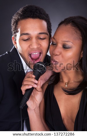 Portrait Of African Couple Singing With Microphone Over Grey Background