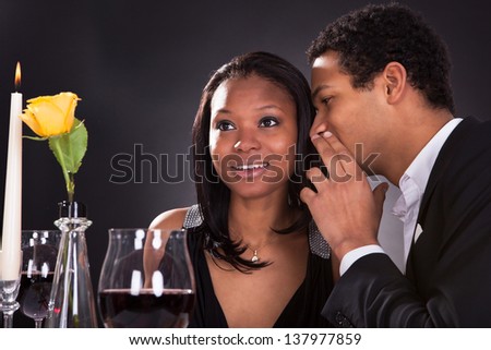 Portrait Of Man Whispering To Girlfriend\'s Ear At Dinner