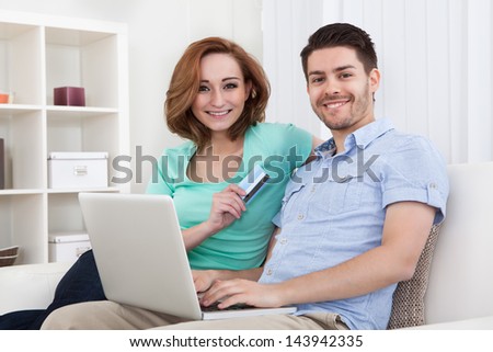 Portrait of young happy couple sitting on couch shopping online