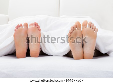 Close-up of couple\'s feet sleeping on bed in bedroom