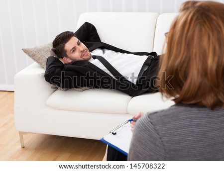 Business man reclining comfortably on a couch talking to his psychiatrist explaining something