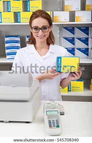 Happy Female Pharmacist Showing Drug In Pharmacy