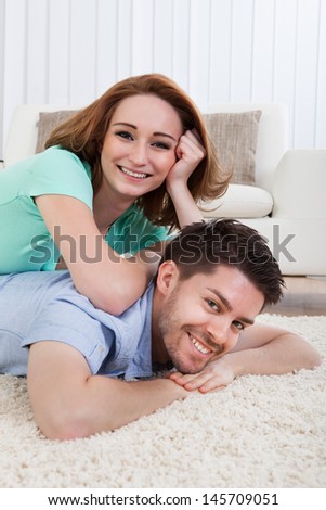 Happy Young Couple Lying On Front Over Carpet