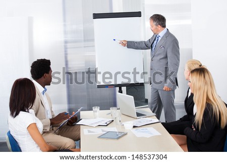 Businesspeople Looking At Businessman Explaining In Presentation