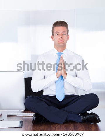 Young Businessman Sitting On Desk Practicing Yoga In Office