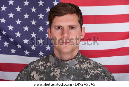 Portrait Of Serious Solider Standing In Front Of Us Flag