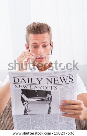 Man Reading Newspaper With The Headline New Layoffs
