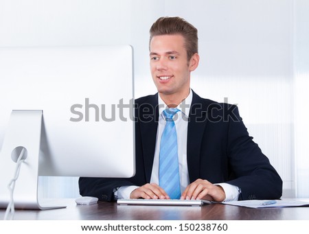 Portrait Of Happy Young Businessman Using Computer In Office