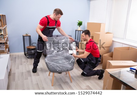 Two Young Male Movers Packing Furniture With Plastic Wrap In Living Room Stock foto © 
