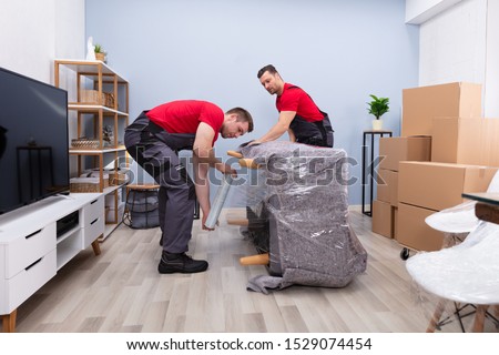 Two Young Male Movers Wrapping The Sofa With Plastic Wrap In Living Room Stockfoto © 