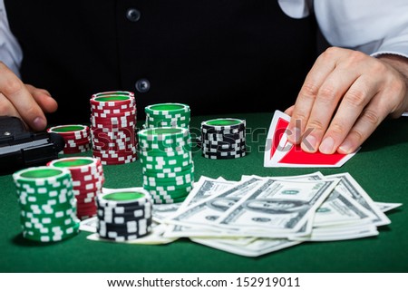 Portrait of a croupier looking at playing cards with gun and stack of token chips on table