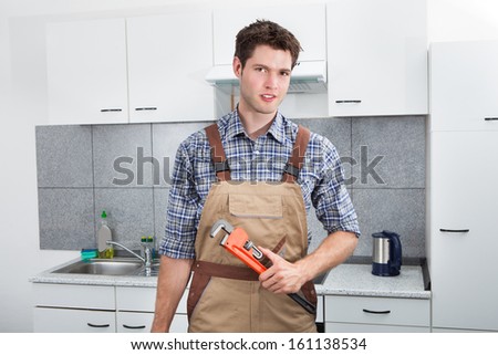 Happy Young Plumber Holding Pipe Wrench In Kitchen Room