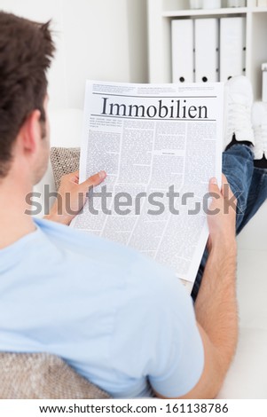 Young Man Reading Newspaper With Real Estate Headline