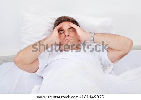 Portrait Of A Young Man Lying On Bed Suffering From Headache