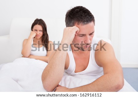 Frustrated Man Sitting On Bed In Front Of Young Woman