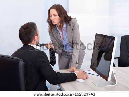 Young Naughty Businesswoman Holding Necktie Of Businessman