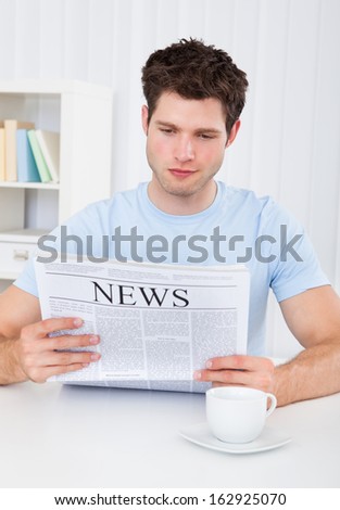 Young cheerful man reading newspaper at home