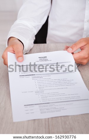 Close-up Of Businessman\'s Hand Holding Resume On Desk