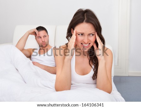 Frustrated Woman Sitting On Bed In Front Of Young Man