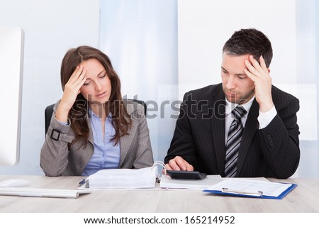 Worried Businessman And Woman Calculating Bills At Desk In Office