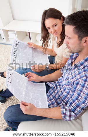 Portrait Of A Happy Young Couple Sitting On Couch Reading Newspaper