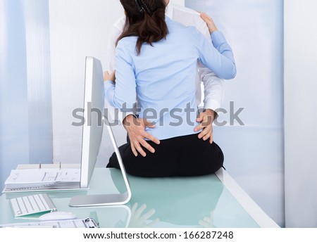 Businessman Embraces A Female Colleague Who Is Sitting Near A Desktop