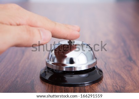 Close-up Of Hand Ringing Service Bell Kept On Wooden Table