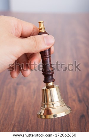 Close-up Of Person Hand On Wooden Table Holding Bell